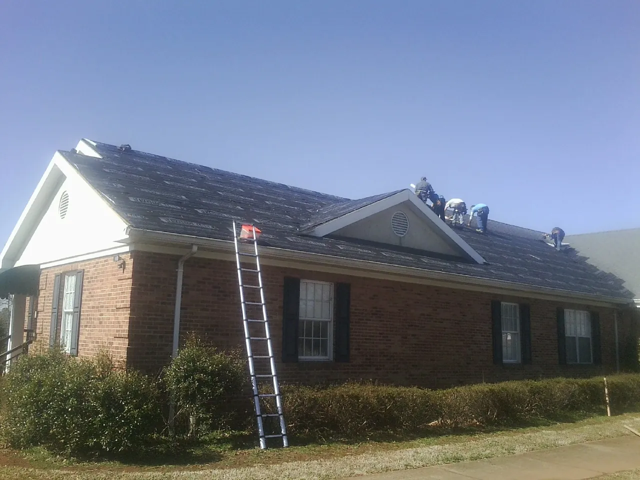 Crew tearing shingles off a brick ranch roof with a ladder set — Metal Roof Repair work by our crew in Exton