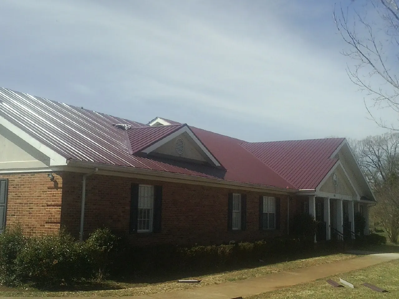 Red metal roof with gabled entries on a long brick building, from a Hail Damage Roof Repair job in Exton